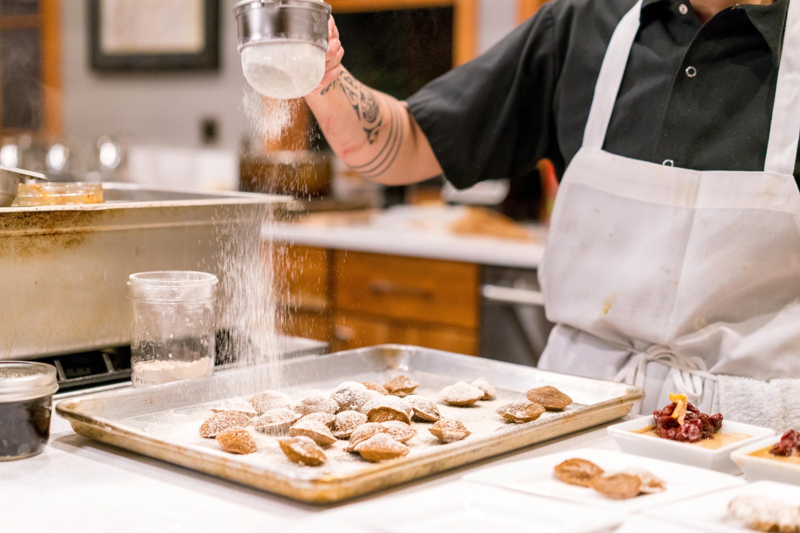 Baker sprinkling flour over cookies