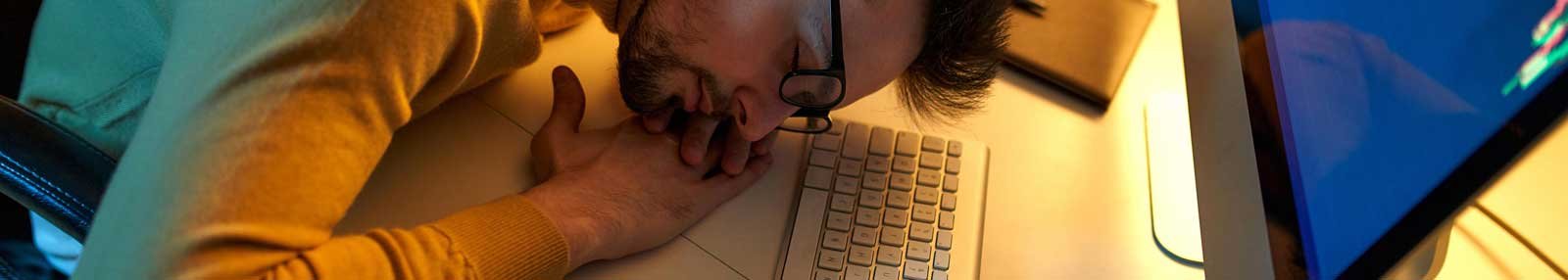A man with glasses sleeping at a table in front of his computer